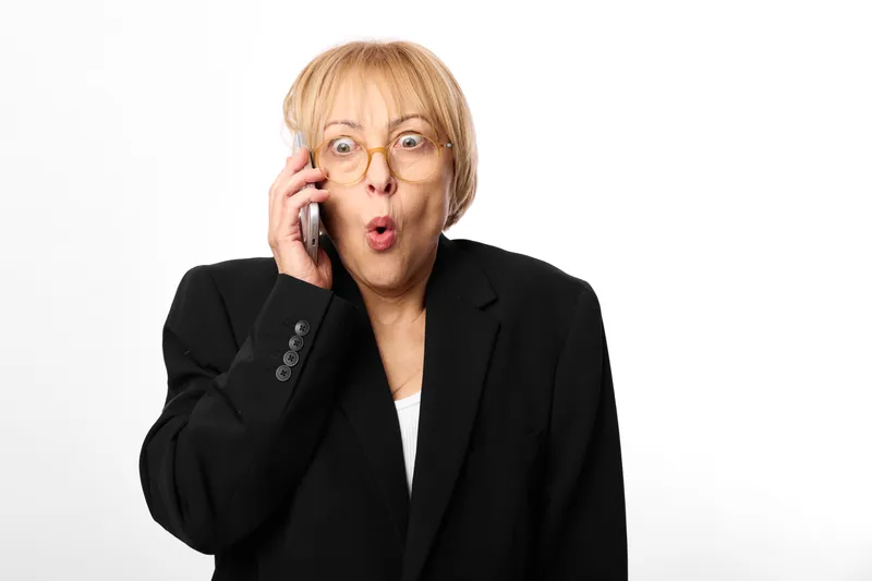 Woman senior glasses blonde surprised call phone communication portrait business, blazer in studio, white background, hand near ear, shocked expression