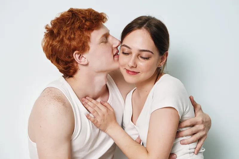 Couple, affection, love, intimacy, redhead, young, relationship, together, emotion, tenderness in casual white clothing hugging and expressing closeness on plain background.