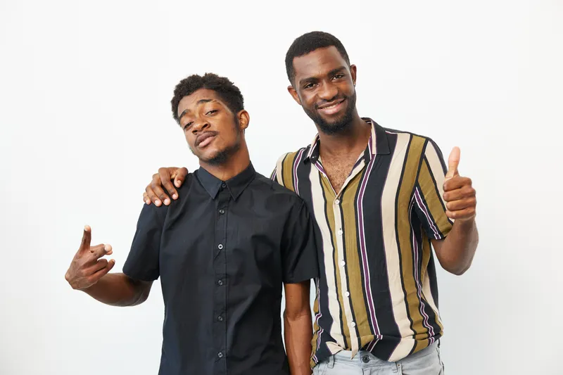 Two smiling African American men pose together, conveying friendship and confidence with their casual attire and joyful expressions.