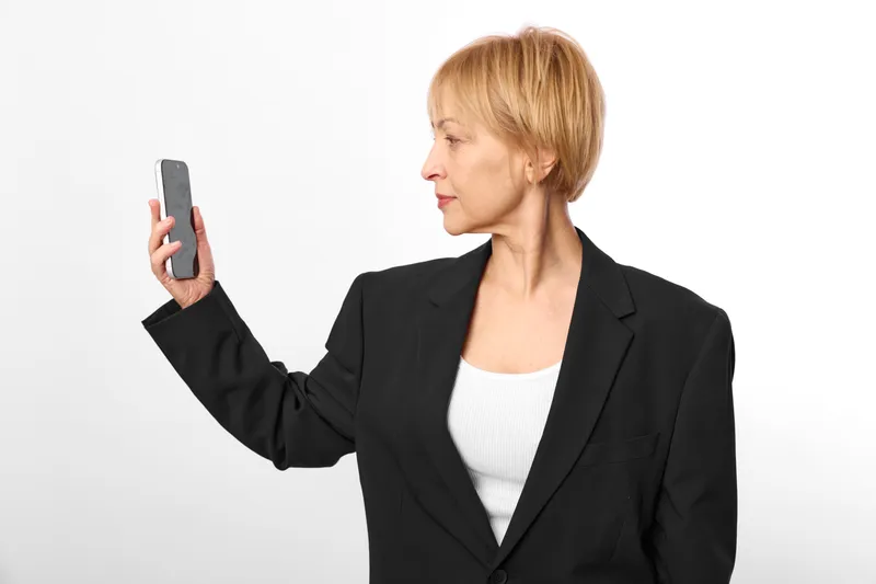 Woman in business suit holding smartphone for communication, modern technology, portrait profile view, smartphone screen visible, studio lighting, calm mood