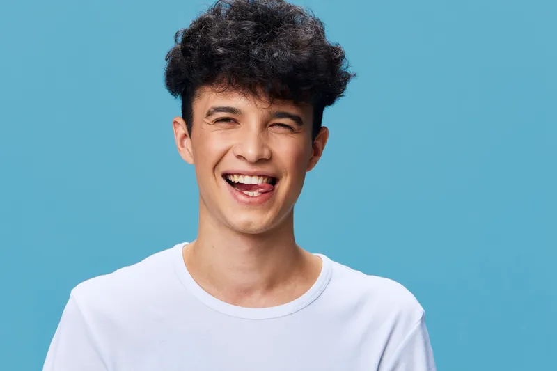 smiling man wearing white t-shirt shows playful expression with tongue out on bright blue background, youthful and cheerful mood portrait, casual style