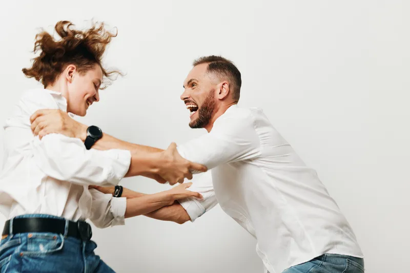 Professional man and colleague clash playfully against a plain colored background, conveying strong emotion and dynamic energy in a business scene that highlights focus, drive, and teamwork.