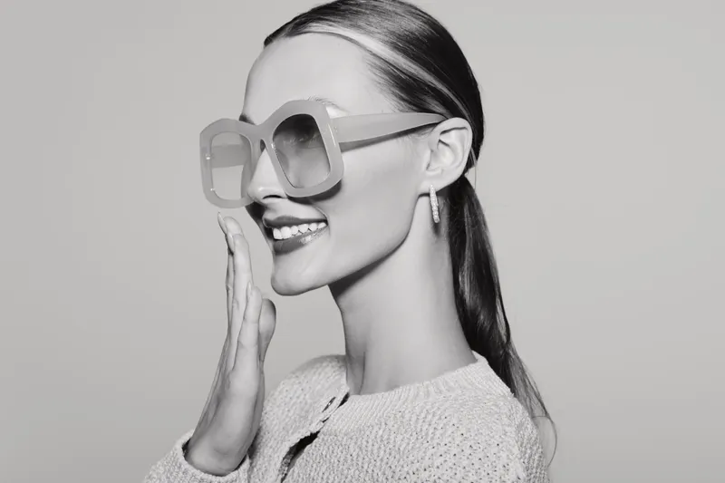 Smiling young caucasian woman with light skin and long hair wearing large sunglasses and knitted sweater in studio. Fashion and lifestyle concept.