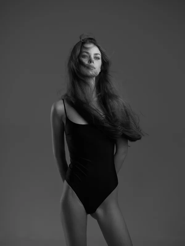 Black and white portrait of a woman in a black swimsuit with flowing hair and a neutral expression.