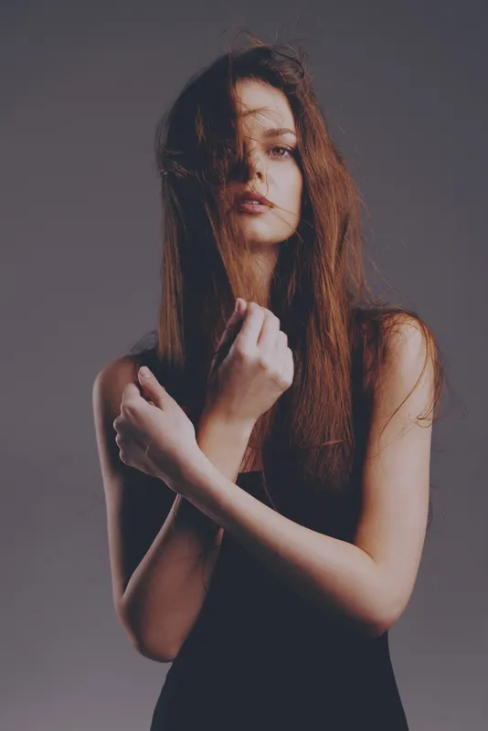 Melancholic woman with long hair in black dress with subdued lighting and muted background