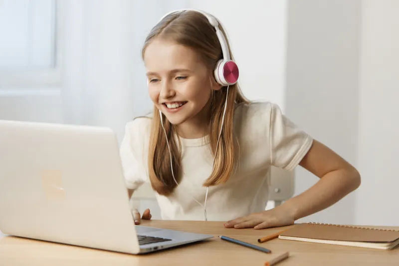 Happy young girl with headphones enjoying online learning at home, focused on her laptop, bright and cheerful atmosphere in a modern interior