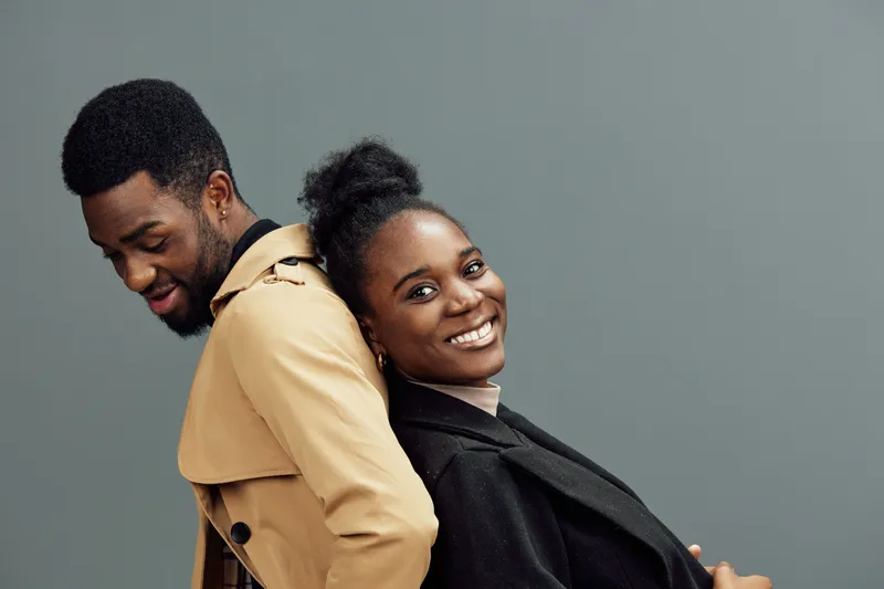 Happy young couple embracing in stylish clothing with a neutral background, showcasing emotions of love and connection through joyful expressions