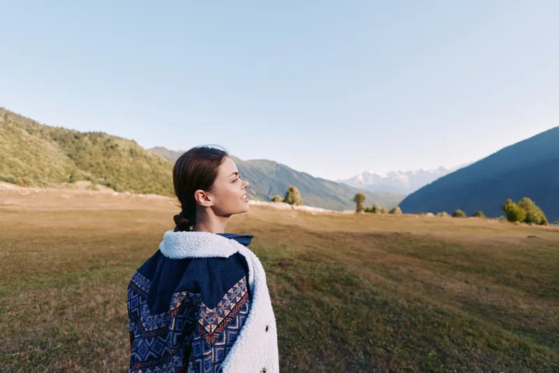 Woman portrait with backpack in mountain landscape and wide meadow, hiking and travel scene at sunrise. Young traveler enjoying nature, panoramic view and outdoor exploration.