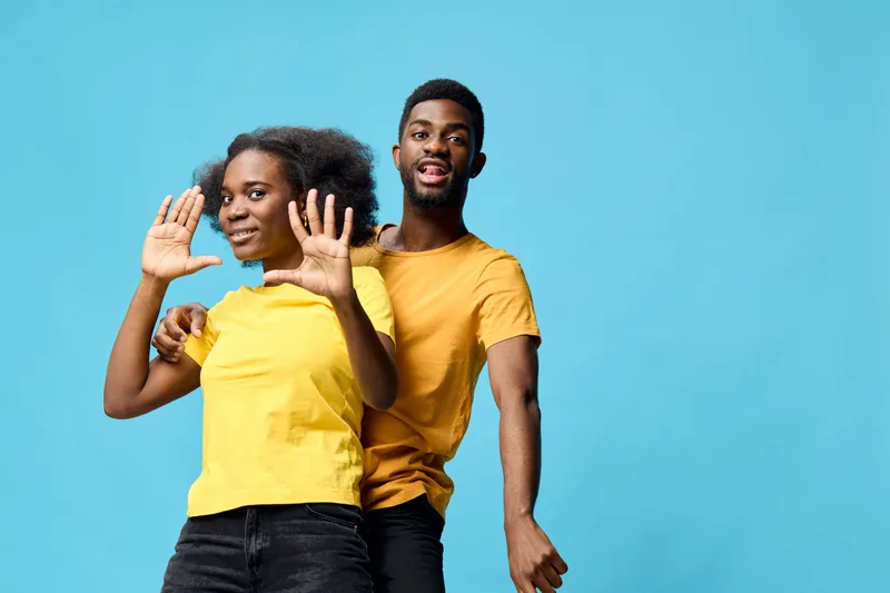 Joyful young couple celebrating together in matching yellow shirts against a vibrant blue background, exuding happiness and playfulness in a fun lifestyle concept