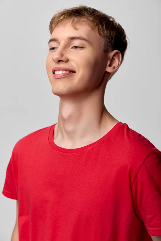 Smiling young man in a red shirt stands against a clean studio backdrop, conveying casual confidence and upbeat mood suitable for lifestyle, fashion, and wellness themes in stock imagery.