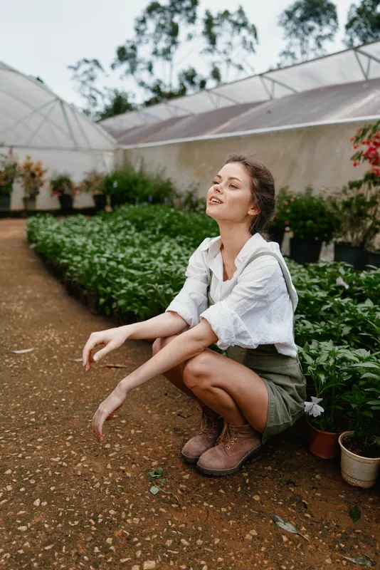 Young woman enjoying nature in a greenhouse, wearing casual attire, showcasing joy and tranquility while surrounded by lush greenery and plants