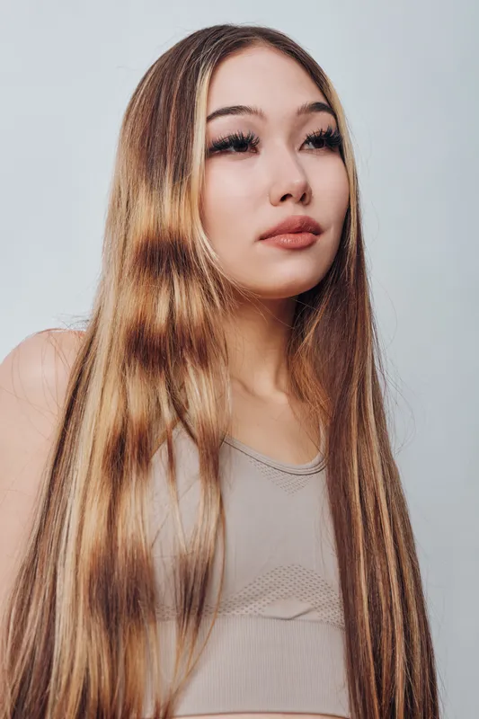 Portrait of young woman with long straight hair wearing sleeveless top looking away on white background, natural makeup and confident expression closeup
