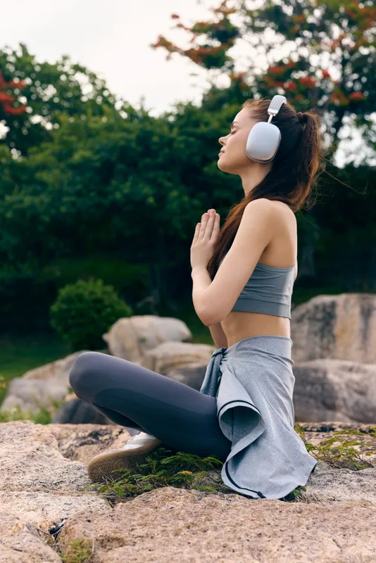 Young Asian woman practicing yoga outdoors with headphones, expressing tranquility and mindfulness in a serene natural setting