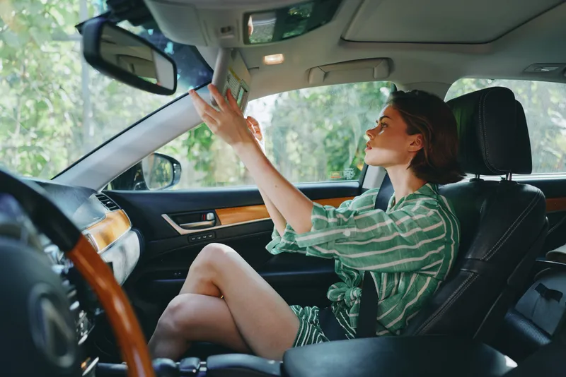 A cheerful woman sits in the driver's seat, smiling and focused on the road ahead.