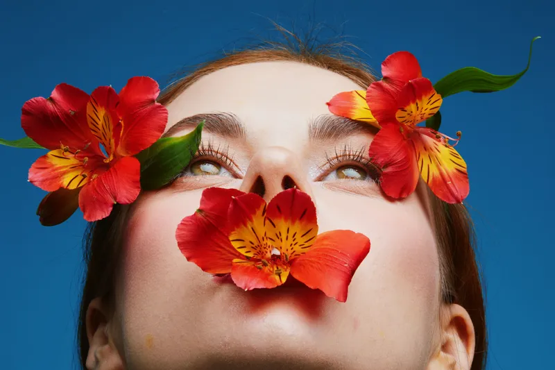 Young woman with vibrant flowers in her hair, showcasing a joyful expression against a bright blue background, representing beauty and nature in a colorful and artistic concept