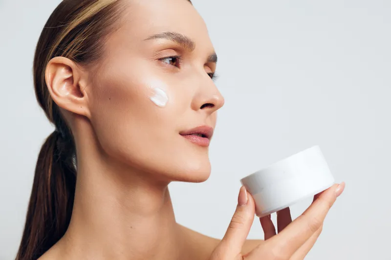 Young woman applying face cream with smooth skin, natural skincare routine, close up portrait, soft lighting, neutral background, beauty concept