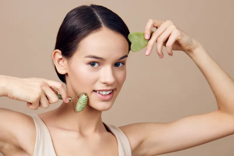 Young woman using jade roller for facial treatment, promoting healthy skincare and relaxation with natural beauty routine