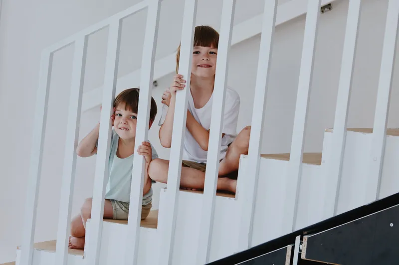 Two cheerful boys playfully interacting at home, sitting on smart white stairs, creating a lively and dynamic atmosphere filled with joy.