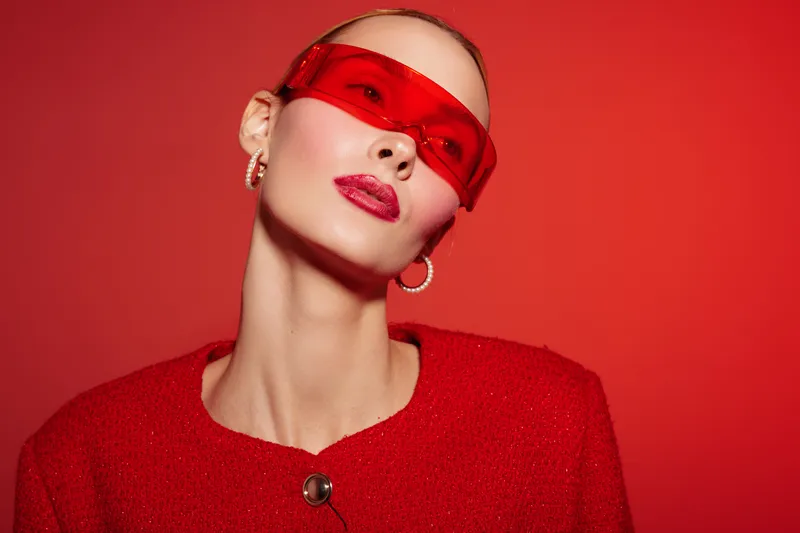Stylish woman in red sunglasses and red outfit poses against red background. Fashion portrait with bold makeup and modern accessories. Concept of style, confidence, and color coordination.