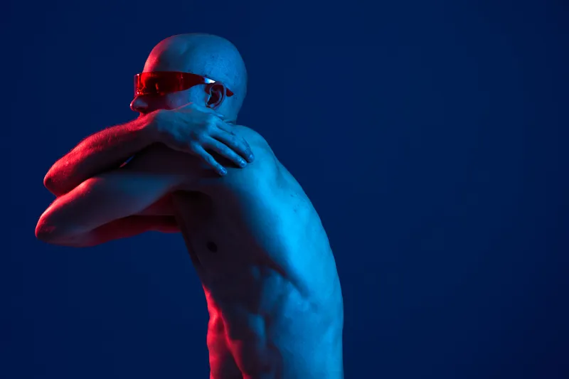 A striking representation of a man posed with an artistic touch, featuring vibrant blue and red lighting in a captivating, minimalist environment.