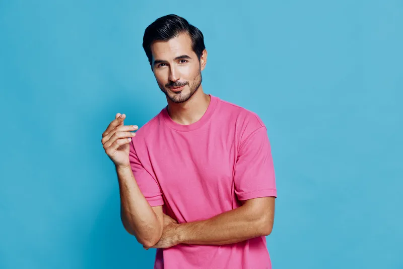 Stylish man posing confidently in a bright pink t-shirt against a vibrant blue background. Casual fashion concept with a touch of charm.