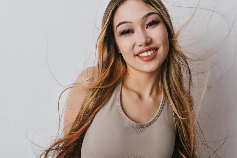 Young woman smiling with long hair and natural makeup wearing sleeveless top against white background in studio portrait. Beauty, happiness and casual style concept.