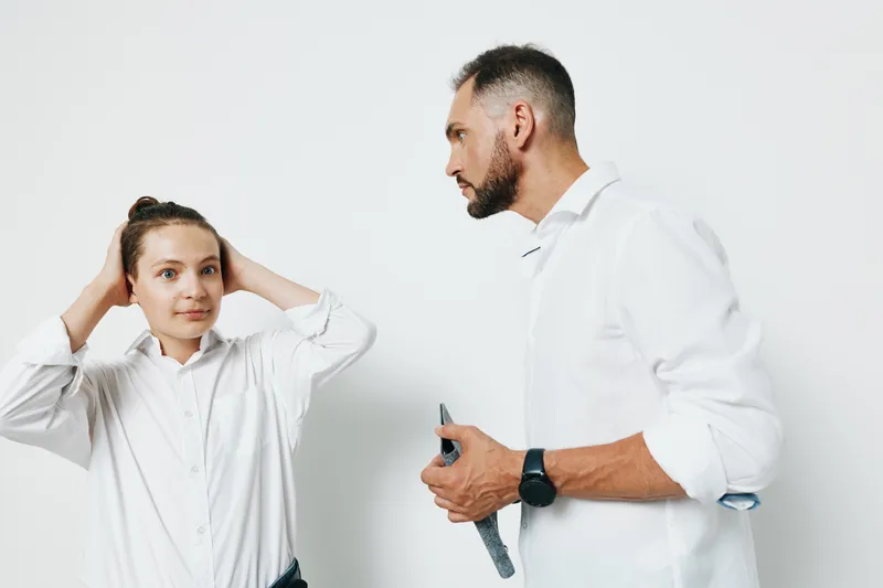 A professional man and a female colleague stand against a plain colored background, exuding focus and calm as they discuss plans, symbolizing teamwork, ambition, and productive dialogue in a business