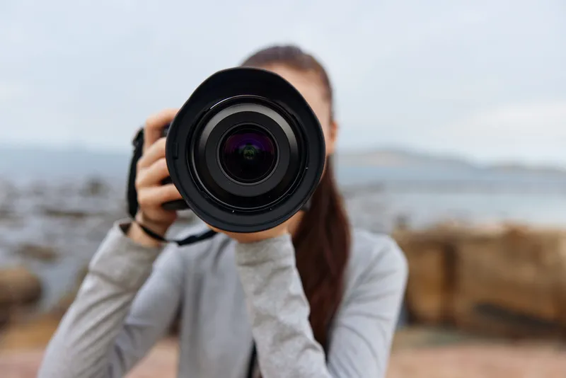 Young woman with a camera at the beach, capturing moments with a professional lens, showcasing passion for photography and creativity