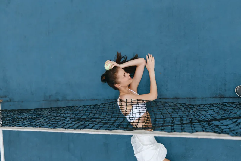 Young woman with long hair brushing her hair while lying on a net against a blue wall, showcasing beauty and relaxation in a bright, stylish environment