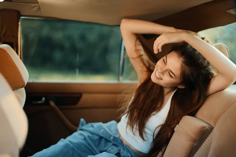 Joyful young woman with long hair enjoying a carefree moment in a vintage car, creating a warm and nostalgic atmosphere with vibrant colors and soft natural light.