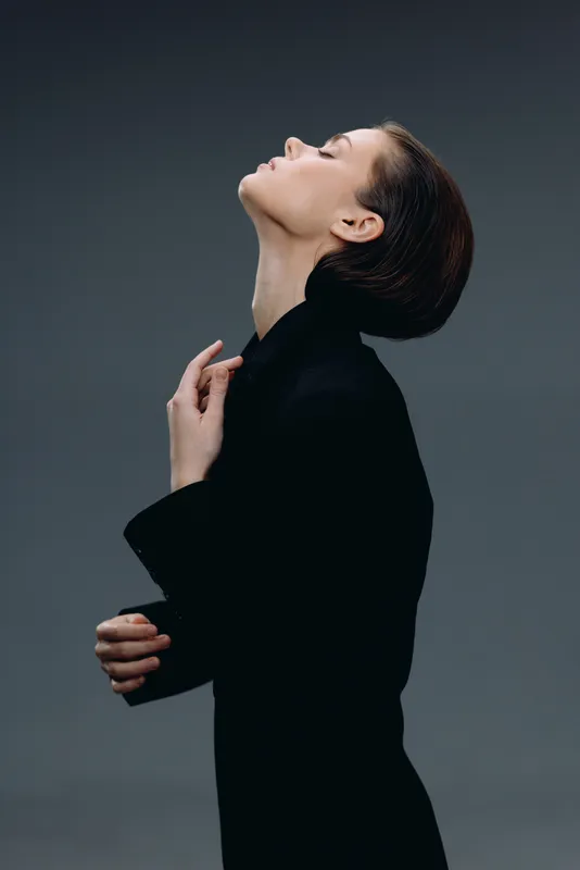 Profile of a woman with short hair in black outfit, expressing calm and elegance against a dark background.