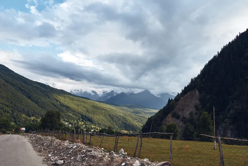 Mountains and valley landscape along a rural road under a dramatic sky with scattered clouds, capturing peaceful countryside and expansive outdoor scenery