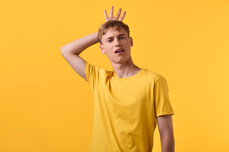 Yellow shirted man raises his hand over his head in front of a bright yellow studio backdrop, casual pose and playful expression creating a bold, energetic lifestyle stock image that highlights color