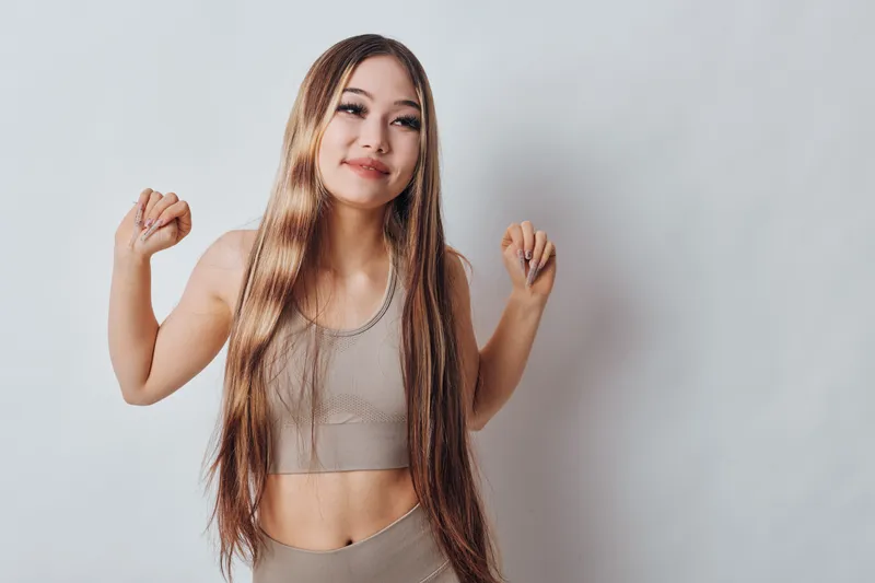 Young woman in sportswear stretching arms and smiling for fitness, health and wellness concept with casual exercise and active lifestyle at home or studio space.