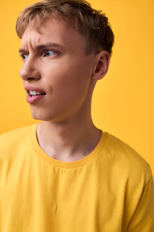 Man wearing a yellow shirt with a puzzled expression against a bright yellow backdrop, close-up studio shot capturing thoughtful, casual mood and facial detail