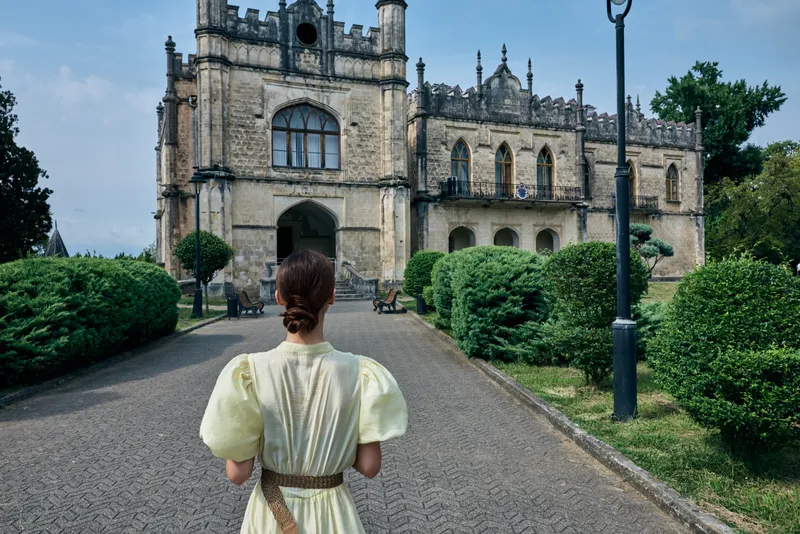 Woman vintage dress backview walking garden walkway historic mansion estate architecture authenticity inclusivity
