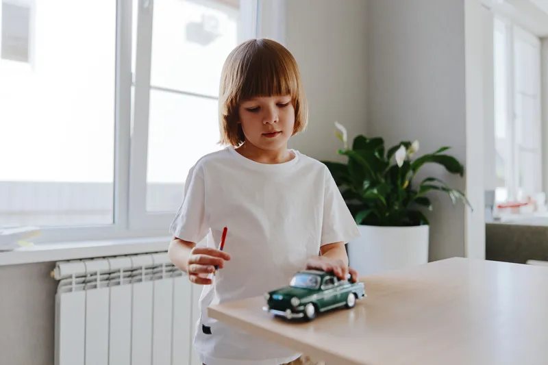 Focused boy playing with a toy car, capturing the essence of childhood curiosity and imagination in a bright indoor setting.