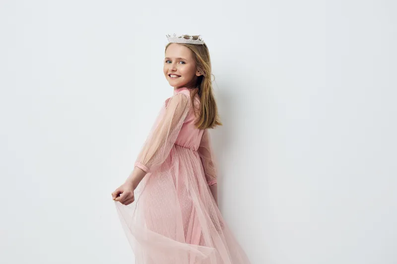 Cheerful young girl in a pink tulle dress and crown, smiling against a clean white background, conveying joy and innocence, perfect for children s fashion