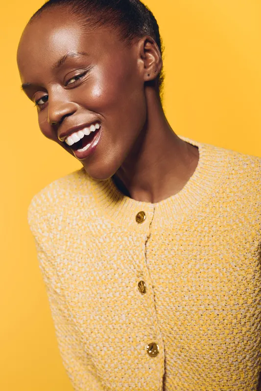 Smiling African woman with dark skin winks at camera wearing yellow knitted sweater. Studio portrait on bright yellow background. Concept of beauty, confidence, and positive mood.