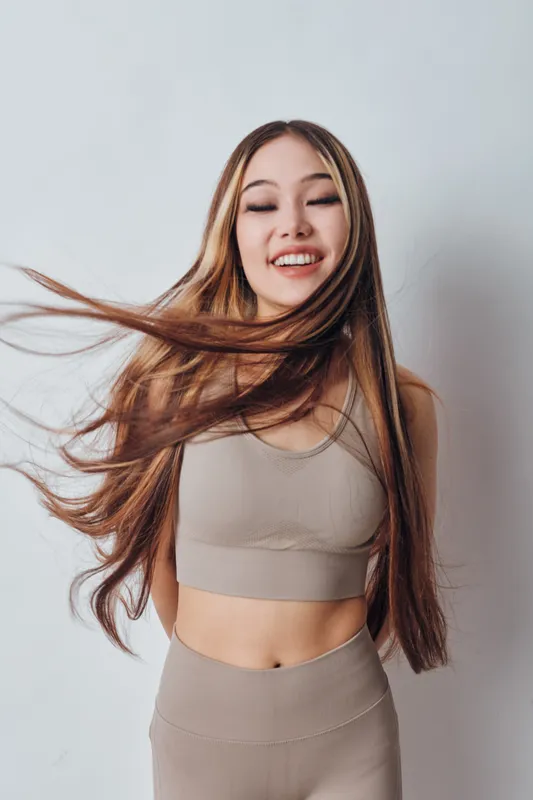 Young woman with long hair in activewear smiling with eyes closed in studio. Fitness, health and lifestyle concept with natural beauty and positive energy.