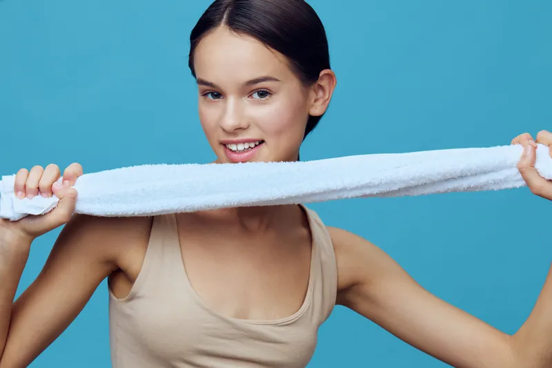 Young model with a towel smiling, showcasing healthy skin and a playful attitude in a blue background, ideal for wellness and beauty themes