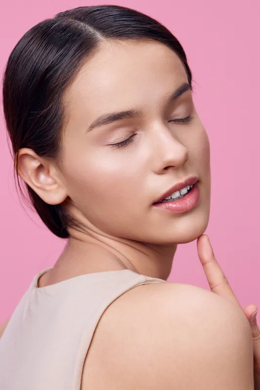 Young female model with closed eyes on a pink background, exuding calmness and confidence, showcasing natural beauty and a relaxed expression