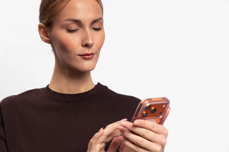 Young woman in dark sweater holding smartphone, looking focused and typing on the screen. Concept for communication, technology use, social media, and mobile interaction.