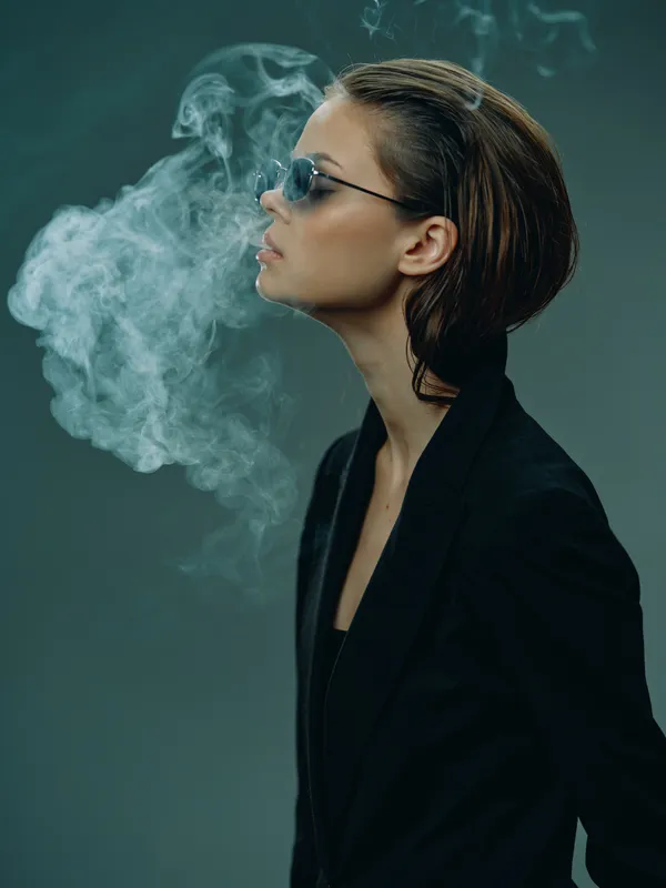 Profile of a stylish woman wearing sunglasses, exhaling smoke with a dark green background