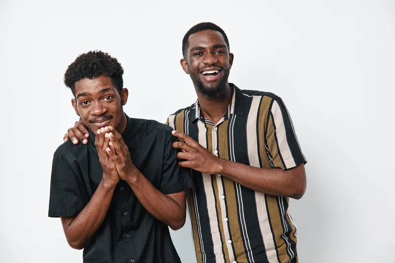 Two young African American men with dark skin smiling and laughing together in casual clothes on white background. Friendship, happiness and positive emotions.