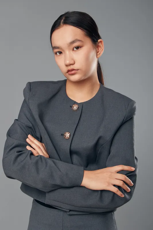 Young Asian woman with serious expression wearing grey business suit standing with crossed arms on grey background. Professional confident businesswoman posing for portrait.