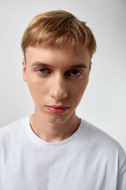 Young man headshot with white shirt against a neutral background, calm expression and blonde hair for clean studio imagery, suitable for fashion, lifestyle and model testing