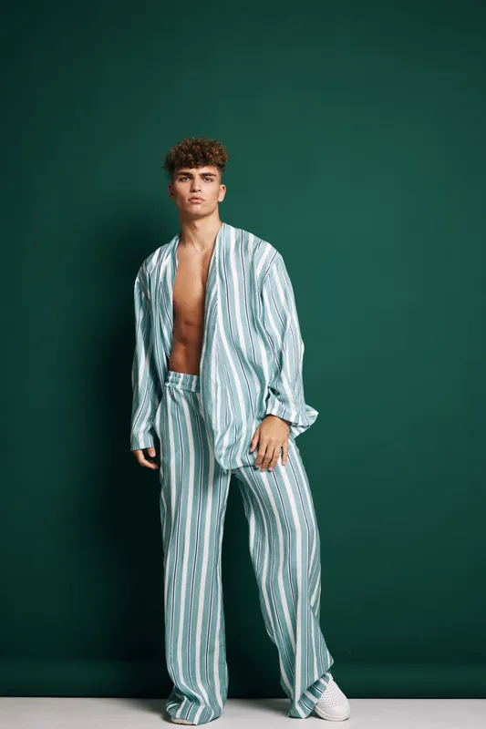 Young man with curly hair posing in stripped green and white discontinued pajamas, casual fashion, stylish apparel, relaxed fit and comfortable outfit on green background in studio