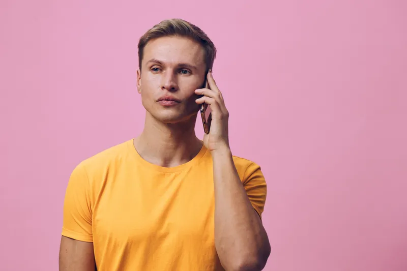 young caucasian man talking smartphone mobile phone yellow t-shirt pink background digital nomad wireless communication technology concept