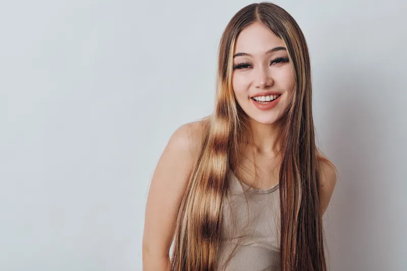 Portrait of young woman smiling with long straight hair wearing casual sleeveless top on neutral background. Female model looking happy and relaxed with natural makeup and friendly expression.